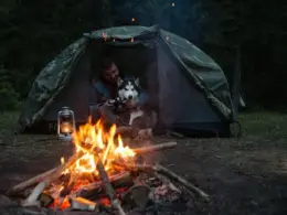 Man and dog in a tent camping during the winter. With campfire and gear.